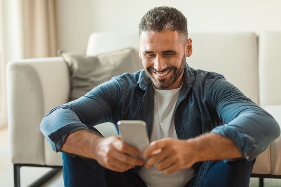 Mann auf dem Sofa lacht über eine Nachricht auf seinem Handy