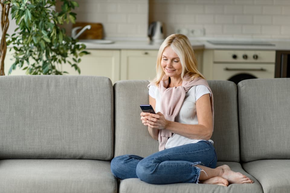 Frau auf dem Sofa schaut lächelnd auf ihr Handy